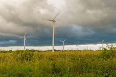 Yenilenebilir enerji kaynaklarından elektrik üreten yel değirmenlerinin manzarası çayır ve bulutların arka planına karşı.
