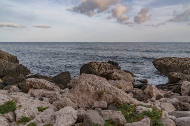 Deniz ufukta dalgaların kıyıya vurduğu kayalık bir sahilden görünüyor.