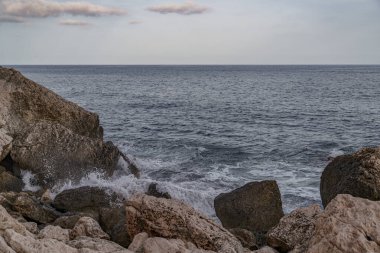 Deniz ufukta dalgaların kıyıya vurduğu kayalık bir sahilden görünüyor.