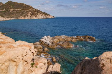 Batan güneş ve ormanlarla aydınlatılan deniz kenarındaki kayalık sahil manzarası.