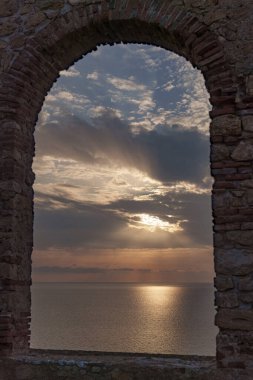 Gün batımında eski tuğla pencerelerden denize bak.