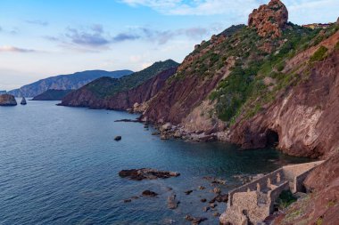 Batan güneş ve ormanlarla aydınlatılan deniz kenarındaki kayalık sahil manzarası.