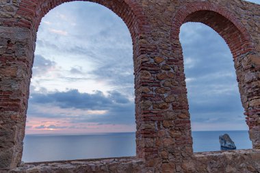 Gün batımında eski tuğla pencerelerden denize bak.