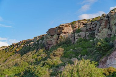 Arkasında güzel bir gökyüzü olan aşırı gelişmiş bir yamaçtan çıkan kayalar.