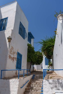 Beyaz duvarlar ve mavi süslemeler arasında merdivenleri olan dar binaların görüntüsü