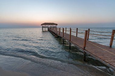 Güneşin doğuşunun güzel manzarası, deniz ufkunun üzerinde gün batımı ön planda bir iskele, denizin bulanık olduğu yerde.