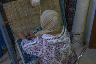 Renkli kıyafetli kimliği belirsiz bir kadın halı dokuyor..