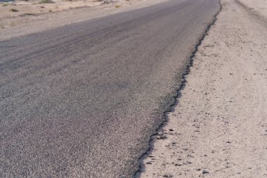 Çölün düz bir bölümünden ufka uzanan asfalt bir yol.