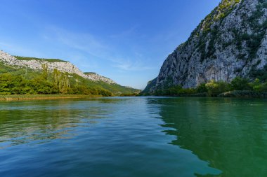 Sakin bir nehrin yüzeyinden kayalık kıyılarına doğru bir manzara.