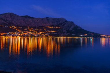 Deniz ve dağların güzel gece manzarası. Işığın suya yansıdığı küçük bir kasaba.
