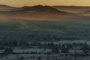 Güneşin doğuşuyla birlikte kışın sisli manzaralı köy evlerinin olduğu sisli bir dağ vadisinin sabah manzarası..