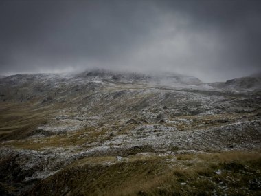 Wide Carpathian plateau with sparse grass, fresh snow, and gray clouds pressing down on wild hills.