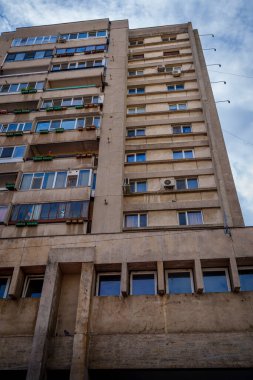 A multi-storey concrete residential building rises against the sky, showing rows of enclosed balconies, air conditioners, and typical utilitarian architecture.