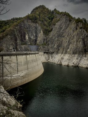 The sweeping concrete arc of Vidraru Dam rises from green waters, surrounded by steep rocky formations in the Carpathians.