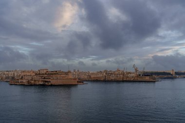 Ditch and massive bastion of Vallettas city fortifications iconic limestone walls and restored dry moat garden beneath clear Mediterranean sky.