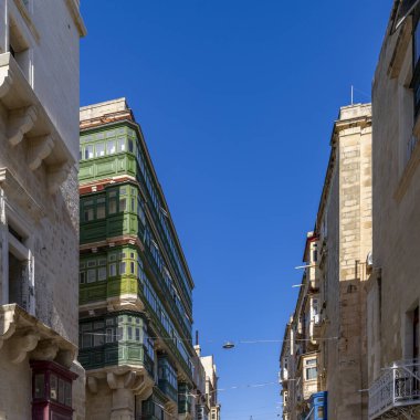 Traditional city scene with green enclosed wooden balconies on historic stone facades in bright sunlight.