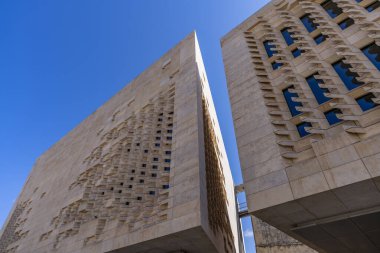 Ditch and massive bastion of Vallettas city fortifications iconic limestone walls and restored dry moat garden beneath clear Mediterranean sky.
