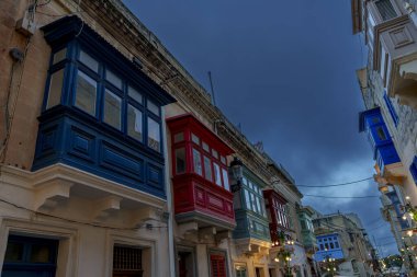 A procession of traditional wooden gallariji painted navy, red, green and blue lines the street, glowing warmly against a dramatic evening cloudbank.