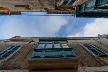 Düşük açılı perspektif, ahşap gallarija ve yüksek açılı kepenkleri yıpranmış taşa karşı vurgular, yukarıdaki parlak bulutlara açılır.