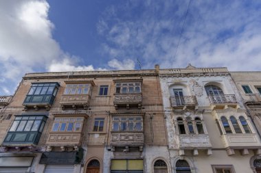 Upward view captures varied gallariji, corbels and stucco details on historic townhouses beneath a bright, cloud-dappled sky.