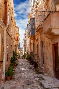 Stone alley lined with peeling walls and small balconies leads to a bright horizon, with puddles reflecting the sky.