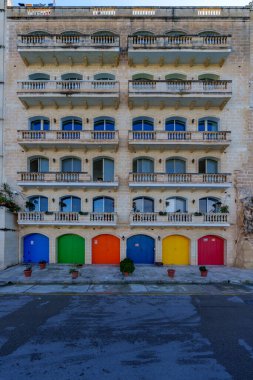 Beş katlı cephede mavi, yeşil, turuncu, lacivert, sarı ve kırmızı renklerde parlak boyanmış garaj kapıları tekrar eden kemerler ve balyalar yer almaktadır..