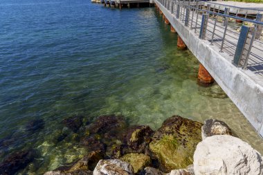 Açısal iskele, şeffaf sığ suların üzerinde uzanır. Mavi limanın yanındaki yosun ve kayaları ortaya çıkarır..