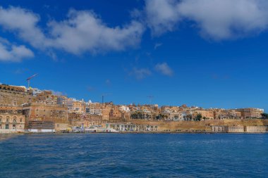 Daytime view across the bay toward Maltas honey colored facades, bastions and waterfront buildings along the shore.