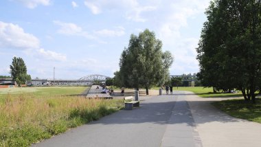 Berlin, Almanya, 14 Temmuz 2023, Berlin 'in popüler bir dinlenme alanı olan Gleisdreieck' teki parkta bir ayak ve bisiklet yolu üzerinde panoramik manzara. Arka planda, yüksek demiryolunun çelik viyakanalları var.