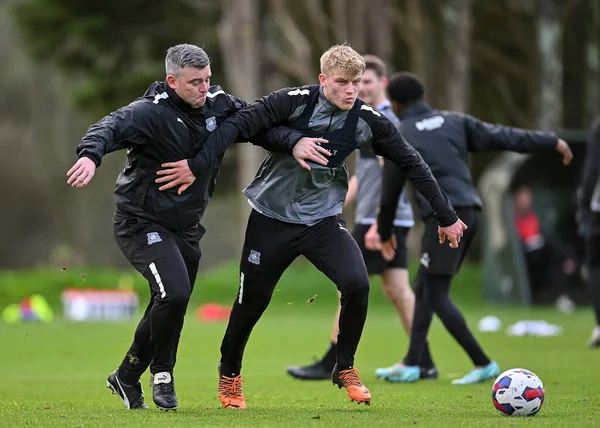 Plymouth Argyle defans oyuncusu Saxon Earley (24), Plymouth Argyle teknik direktörü Steven Schumacher 'ın yanından geçiyor ve Plymouth Argyle antrenmanı sırasında Plymouth Argyle antrenman sahasında çekim yapıyor.