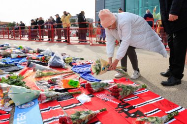 Bir bayan, Sör Bobby Charlton anısına 23 Ekim 2023 'te Old Trafford, Manchester, İngiltere' nin dışındaki Trinity heykeline çiçek bırakıyor.