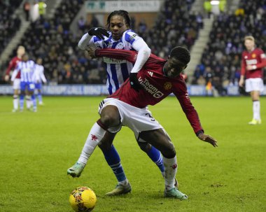 Wigan Atletizm takımından Martial Godo, 8 Ocak 2024 'te Wigan, İngiltere' deki Wigan Stadyumu 'nda oynanan üçüncü tur Dünya Kupası karşılaşmasında Manchester United takımından Kobbie Mainoo ile birlikte top için yarışıyor.