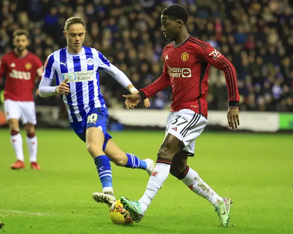 Manchester United takımından Kobbie Mainoo, 8 Ocak 202 'de Wigan, İngiltere' deki Wigan Stadyumu 'nda oynanan ve Wigan FA Cup' ta oynanan üçüncü tur karşılaşmasında Wigan Atletizm takımından Thelo Aasgaard 'ı geçmeye çalışıyor.