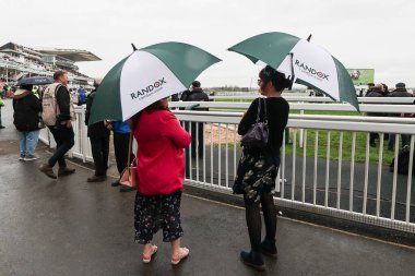 Yarışçılar, 11 Nisan 202 'de Aintree Yarış Pisti, Liverpool' da düzenlenen Randox Grand National 2024 Açılış Günü sırasında şemsiyeler altında yağmurdan korunuyorlar.