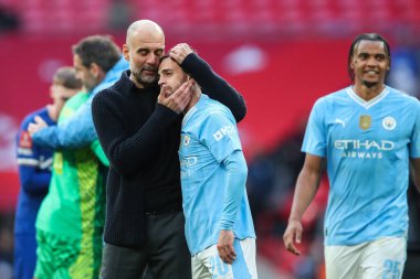 Manchester City 'den Pep Guardiola teknik direktörü ve Manchester City' den Bernardo Silva, 20 Nisan 202 'de Wembley Stadyumu' nda Manchester City 'nin Chelsea' ye karşı oynadığı yarı final karşılaşmasını kazandıktan sonra, takımlarının takımlarını kucaklıyor.