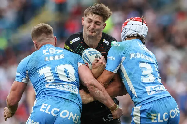 stock image Sam Walters of Wigan Warriors is tackled by Matty Lees of St. Helens and Harry Robertson of St. Helens during the Magic Weekend match Wigan Warriors vs St Helens at Elland Road, Leeds, United Kingdom, 17th August 2024