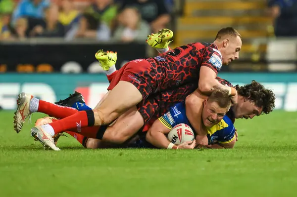 stock image Luke Yates tackled by Frankie Halton of Leigh Leopards and Robbie Mulhern of Leigh Leopards during the Betfred Super League Round 24 match Leigh Leopards vs Warrington Wolves at Leigh Sports Village, Leigh, United Kingdom, 30th August 2024