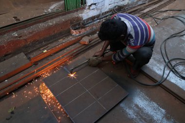 Bir işçi, 19 Aralık 2024 Perşembe günü Hindistan 'ın Kolkata kentindeki bir çelik ve demir toptancısının yanındaki bir demir tabağı kesiyor.. 