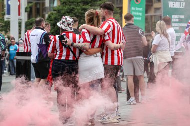 24 Mayıs 2025 'te Wembley Stadyumu' nda Sheffield United 'a karşı Sunderland' ın oynadığı Gökyüzü İddia Şampiyonası Playoff Finali öncesinde fotoğraf çeken Sunderland taraftarlarının arkasında kırmızı bir işaret fişeği var.