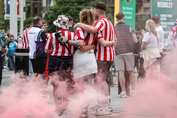 24 Mayıs 2025 'te Wembley Stadyumu' nda Sheffield United 'a karşı Sunderland' ın oynadığı Gökyüzü İddia Şampiyonası Playoff Finali öncesinde fotoğraf çeken Sunderland taraftarlarının arkasında kırmızı bir işaret fişeği var.