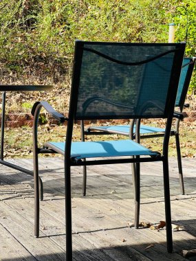 Iron patio furniture set of table, chairs and umbrella. It is on a wooden deck in a sunny, small and private back yard. The fabric is sky blue or turquoise and the umbrella is closed.