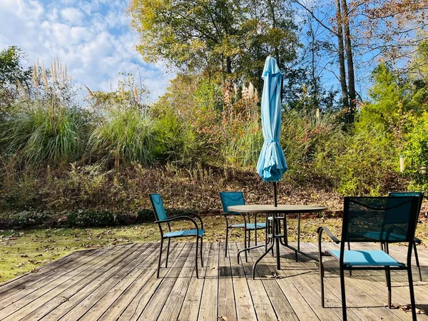 Iron patio furniture set of table, chairs and umbrella. It is on a wooden deck in a sunny, small and private back yard. The fabric is sky blue or turquoise and the umbrella is closed.