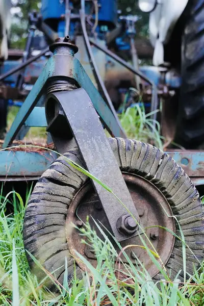 一辆蓝色的老农场拖拉机停在一些树下的田边 它似乎坏了 已经废弃了 — 图库照片