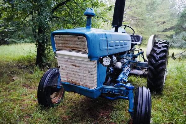 一辆蓝色的老农场拖拉机停在一些树下的田边 它似乎坏了 已经废弃了 — 图库照片