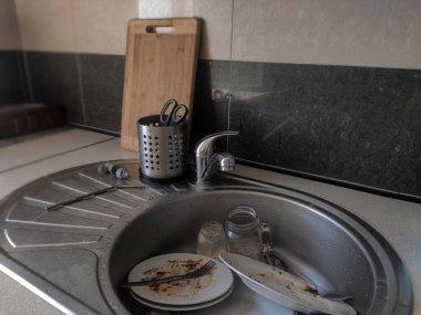 Kirli mutfaktaki su musluğunun altındaki metal lavaboda bir yığın kirli Çin tabağı var..
