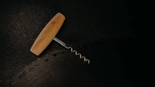Wooden corkscrew for a bottle of wine on a dark background with drops. View from above. Background for text on the theme of wine and wine production