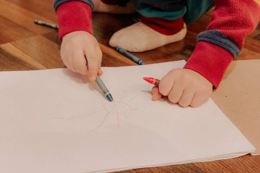 Sevimli küçük çocuk yere uzanıyor ve renkli kalemlerle resim çiziyor. Çocuk hobileri. Erken gelişim, çocuklar için çizimler