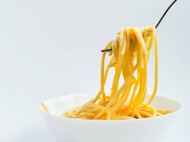 Beyaz arka planda izole edilmiş beyaz tabakta çatallı sossuz spagetti. Un ürünleri, çatalda asılı uzun makarna, glüten ve dengeli beslenme.