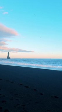 Hofn, İzlanda 'da, siyah plaj, kum ve Vestrahorn dağlı bir günbatımı sahnesinin dikey videosu. Turistler arasında popüler bir yer, büyük dalgalar altında siyah bir sahil ve pembe bir günbatımı. İzlanda, Vik.