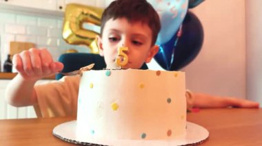 Çocuk pastaya mum üflüyor. Doğum günü ya da pastalı mutlu bebek, balonlu ev partisi. Sevimli çocuk kaşıkla tatlı yiyor. 5 yıllık güzel bir pasta ve mum.